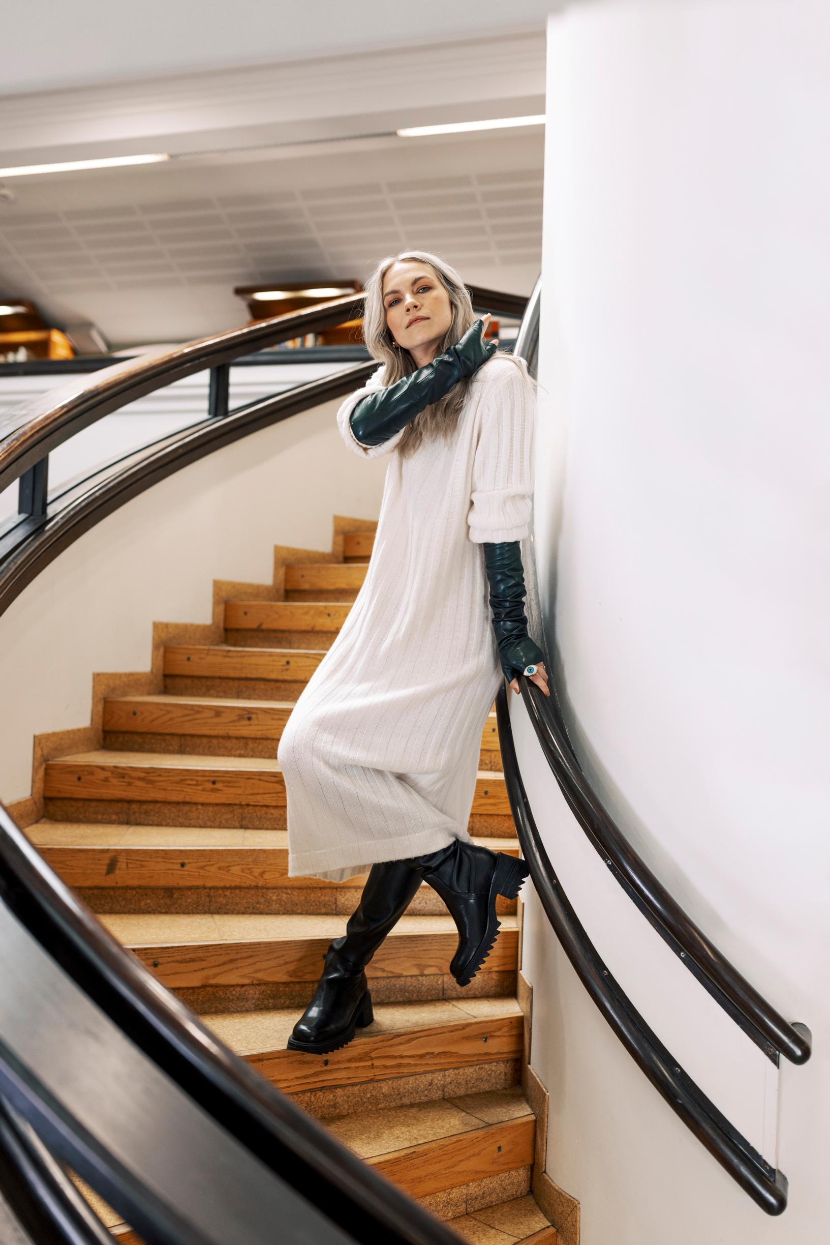 Emmi-Liia Sjöholm portaikossa asunaan neulemekko, pitkät käsineet ja saappaat.