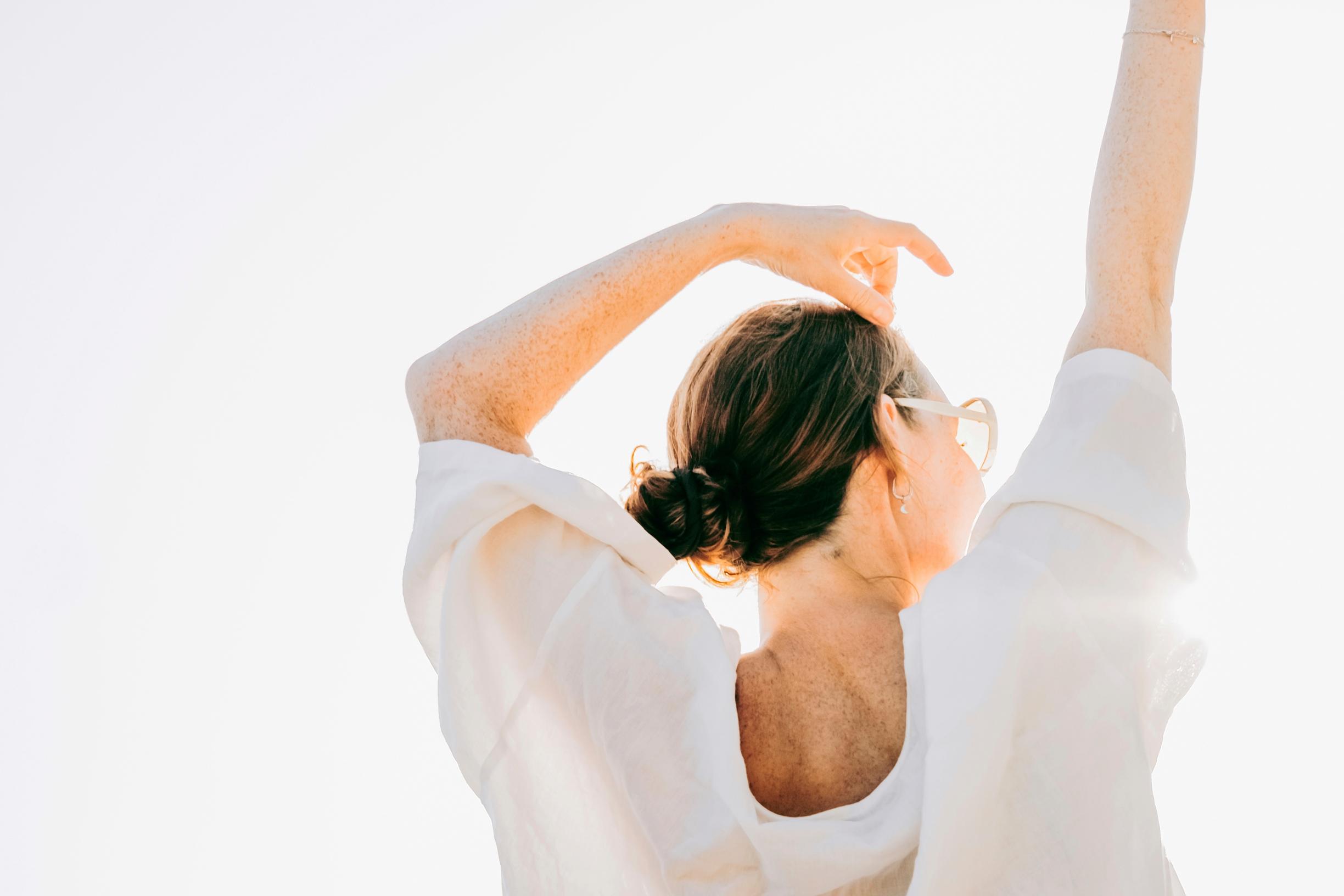 Nainen venyttelee auringossa selkä kameraan