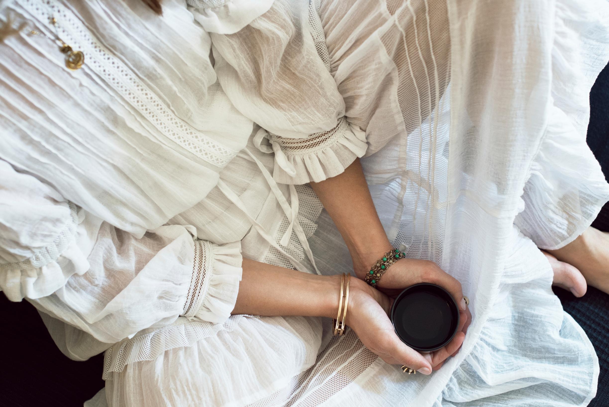 Nainen istuu lattialla kahvikuppi kädessään.