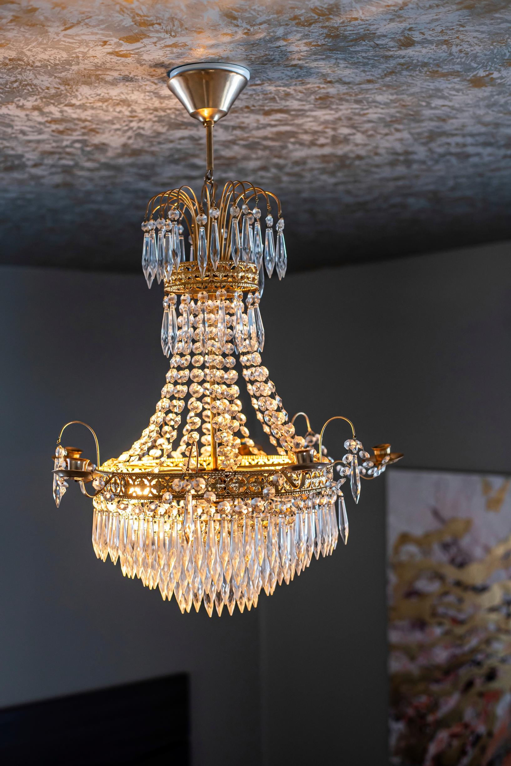 Hannahin makuuhuoneen kristallikruunun hehkuva valo korostaa kauniisti harmaalla ja kultaisella maalattua huonetta.