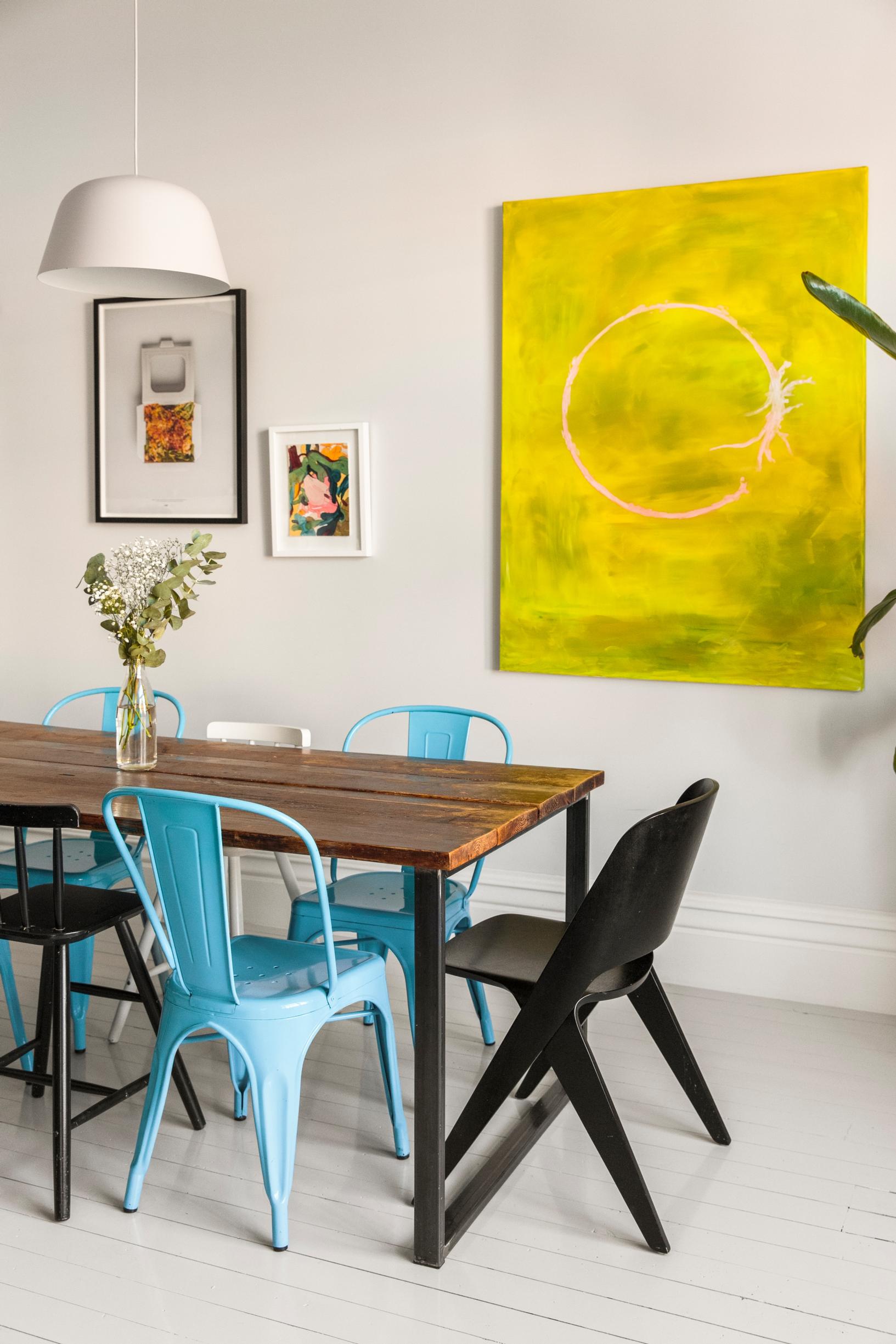 Keittiön pöytä teetettiin Lontoossa puusepällä monta vuotta sitten. Siniset Tolix-tuolit viehättivät aikoinaan värinsä tähden. Ison taulun Karoliina maalasi lahjaksi miehelleen.