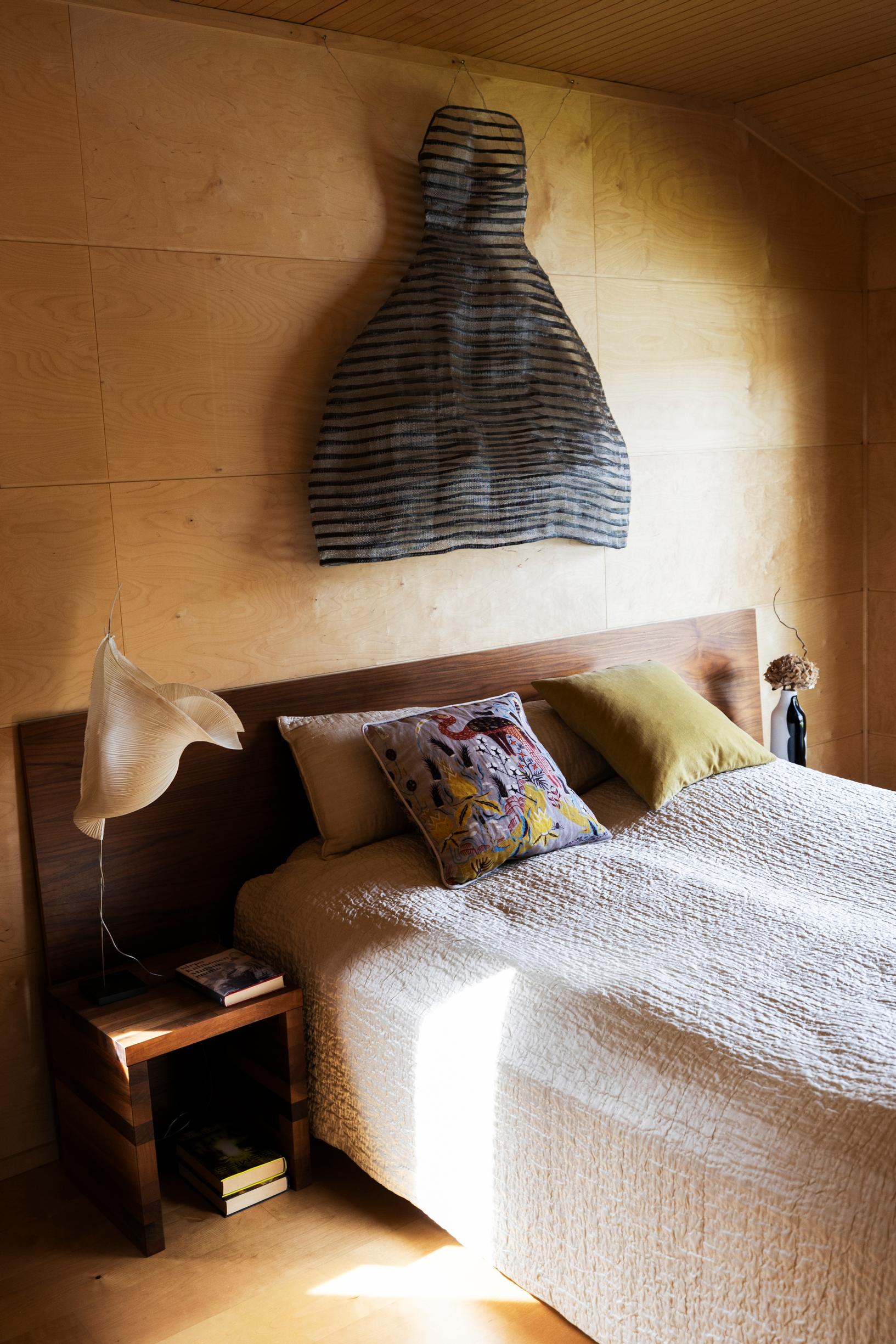 Ritva-Liisan ja Yrjön sänkyä peittää Luhta Homen silkkipeitto. Yöpöydällä on Ingo Maurerin valaisin ja seinällä Ritva-Liisan teräslangasta ja paperinarusta suunnitteleman mekon prototyyppi.