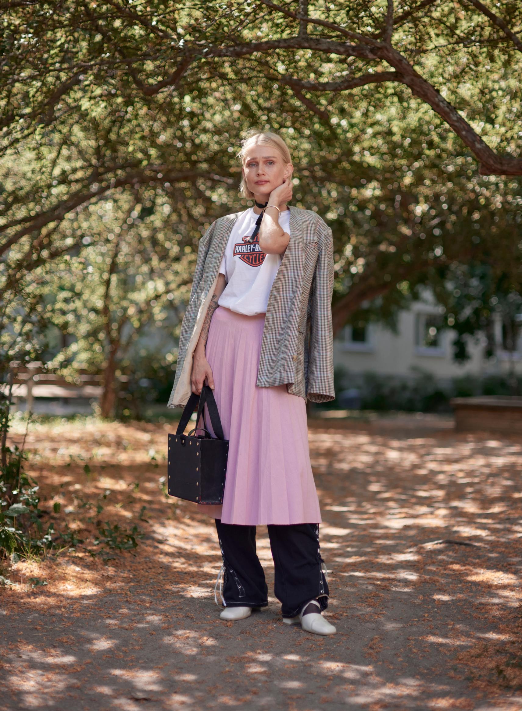 ”Tämän asun kaikki vaatteet on ostettu käytettyinä kirpputorilta. Housut hameen alla on lempiyhdistelmäni. Harley-Davidson paita on hyvä vastakohta ruutujakulle, samoin reisitaskuhousut vaaleanpunaiselle hameelle. Korkokengät puen sukkien kanssa. Kaulaan olen sitonut narun yksityiskohdaksi. Housut ovat monikäyttöiset, sillä niiden leveyttä voi muuttaa nyöreillä.”